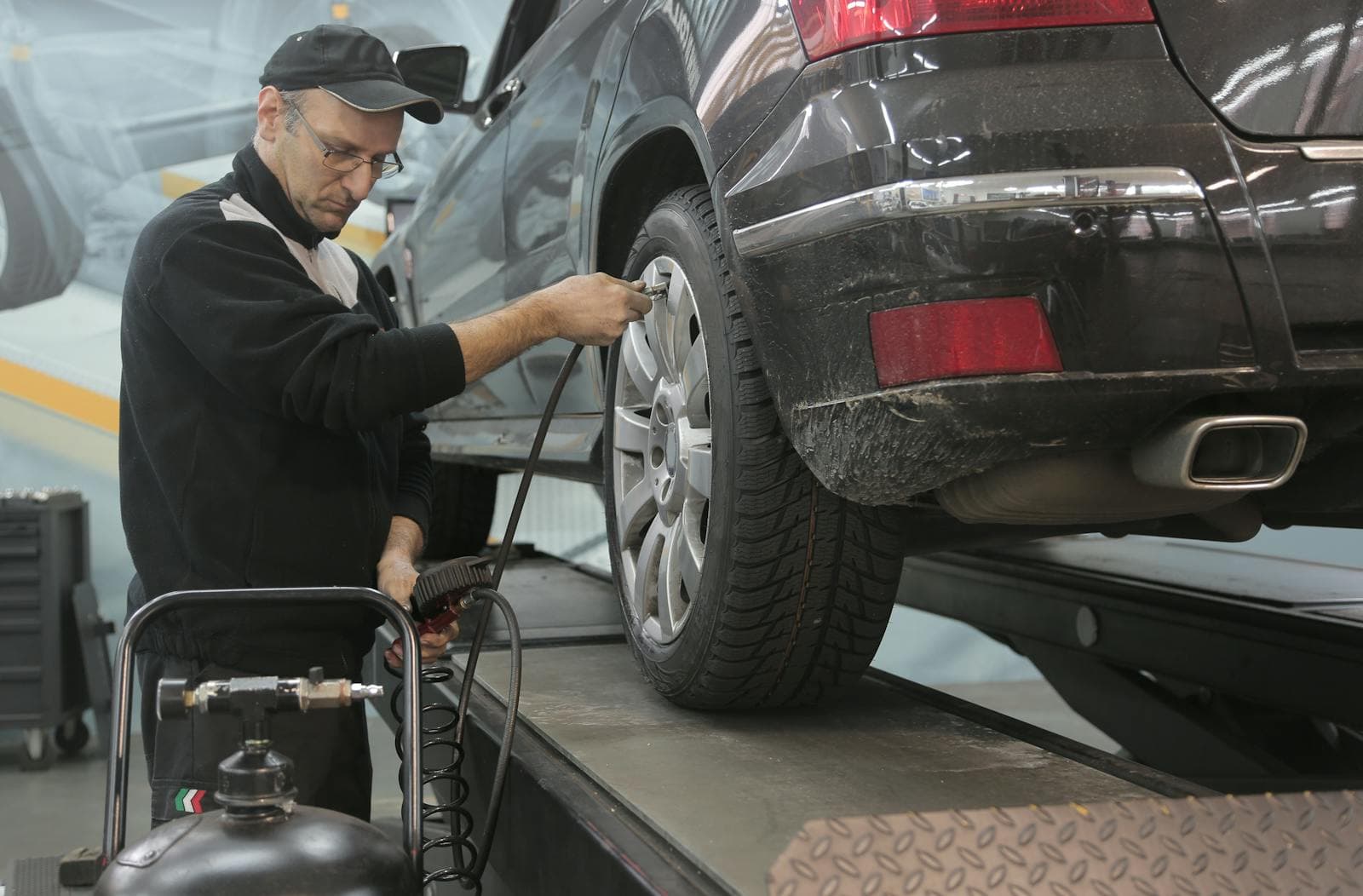 Technician checking tyre pressure with an air line on a raised car