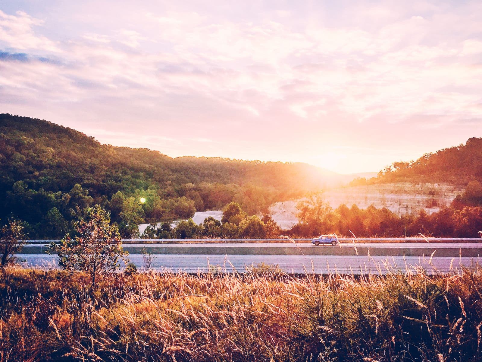 Car on a highway winding through hills at sunset