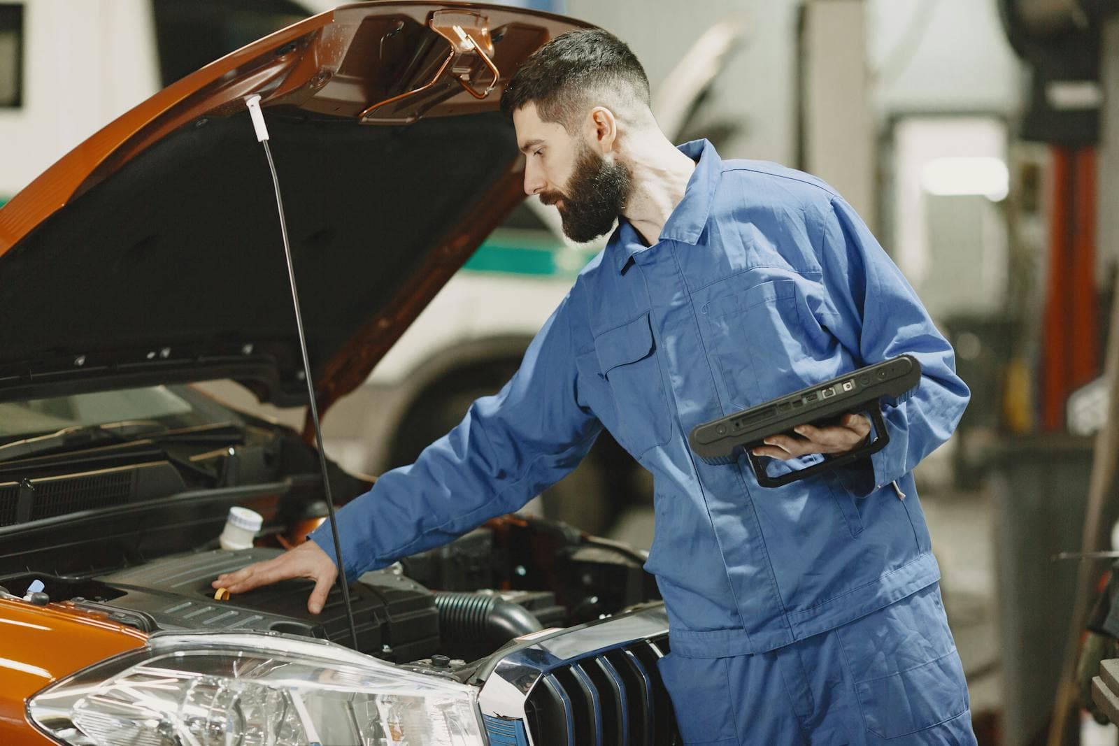 Mechanic with a diagnostic tablet checking under the bonnet of a car